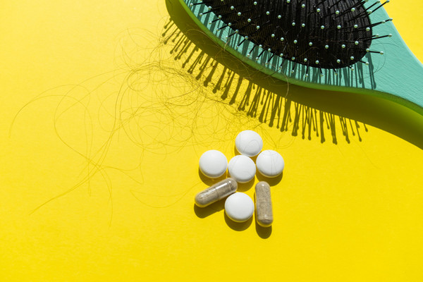 Green comb, pills and fallen hair on a yellow background. Baldness and hair loss problem