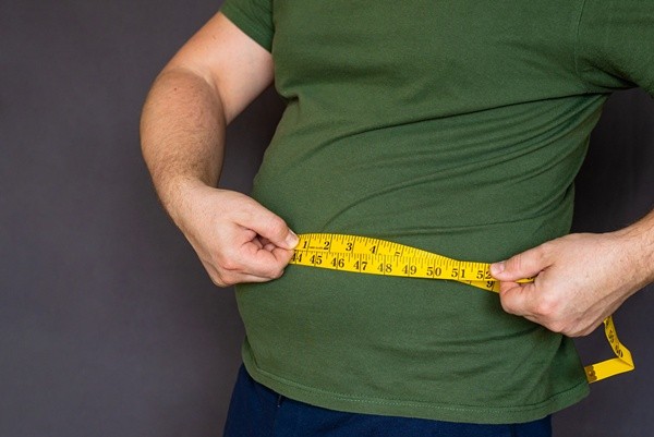 Overweight man in green shirt using a yellow measuring tape to check belly size for weight loss and health monitoring